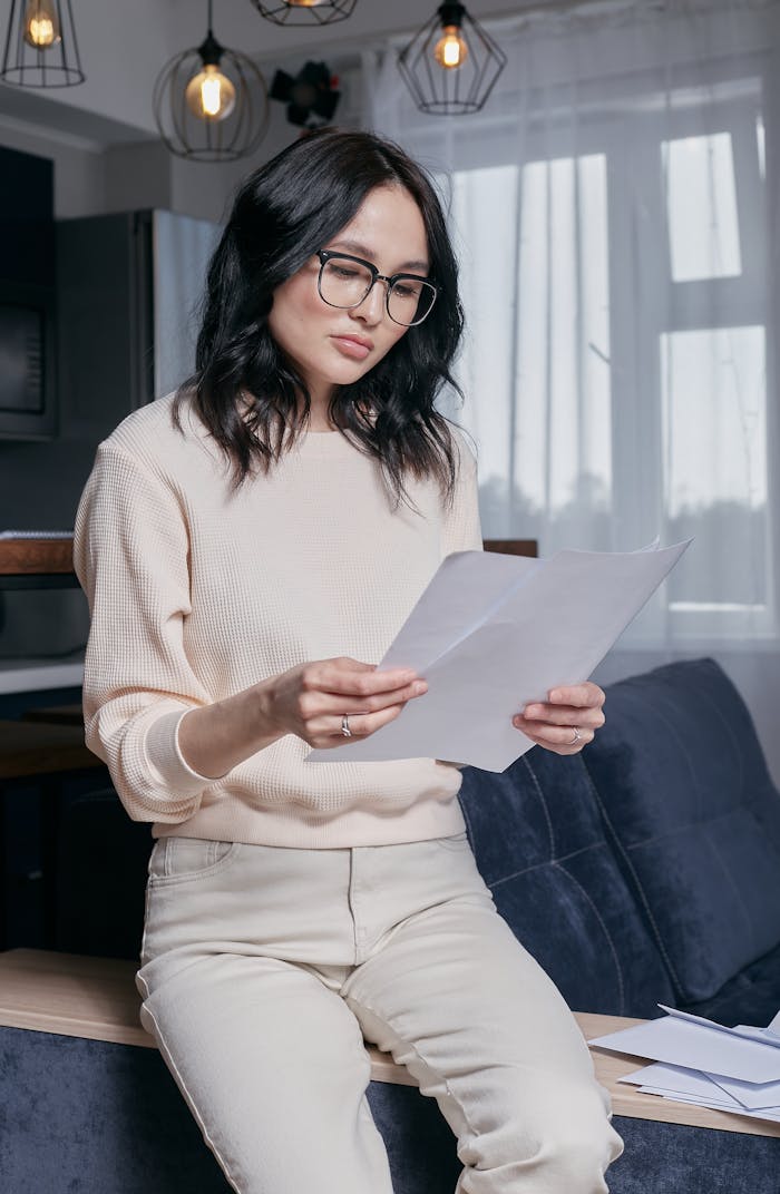our-story Concentrated young woman with glasses reading financial papers in a modern living room.