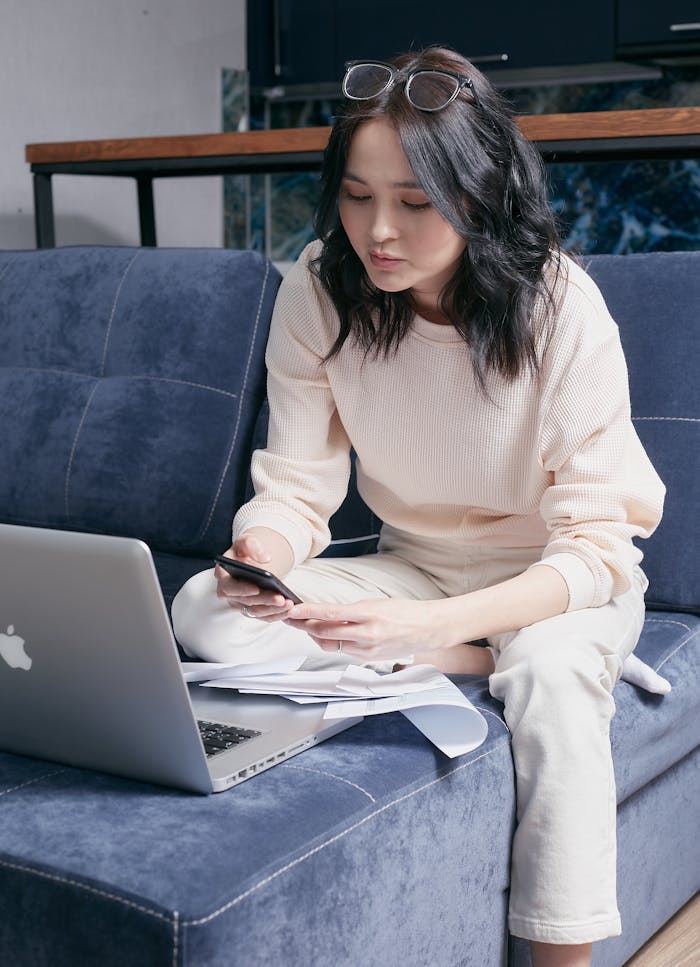 heros-img A young woman sits on a sofa managing her bills with a laptop and smartphone.